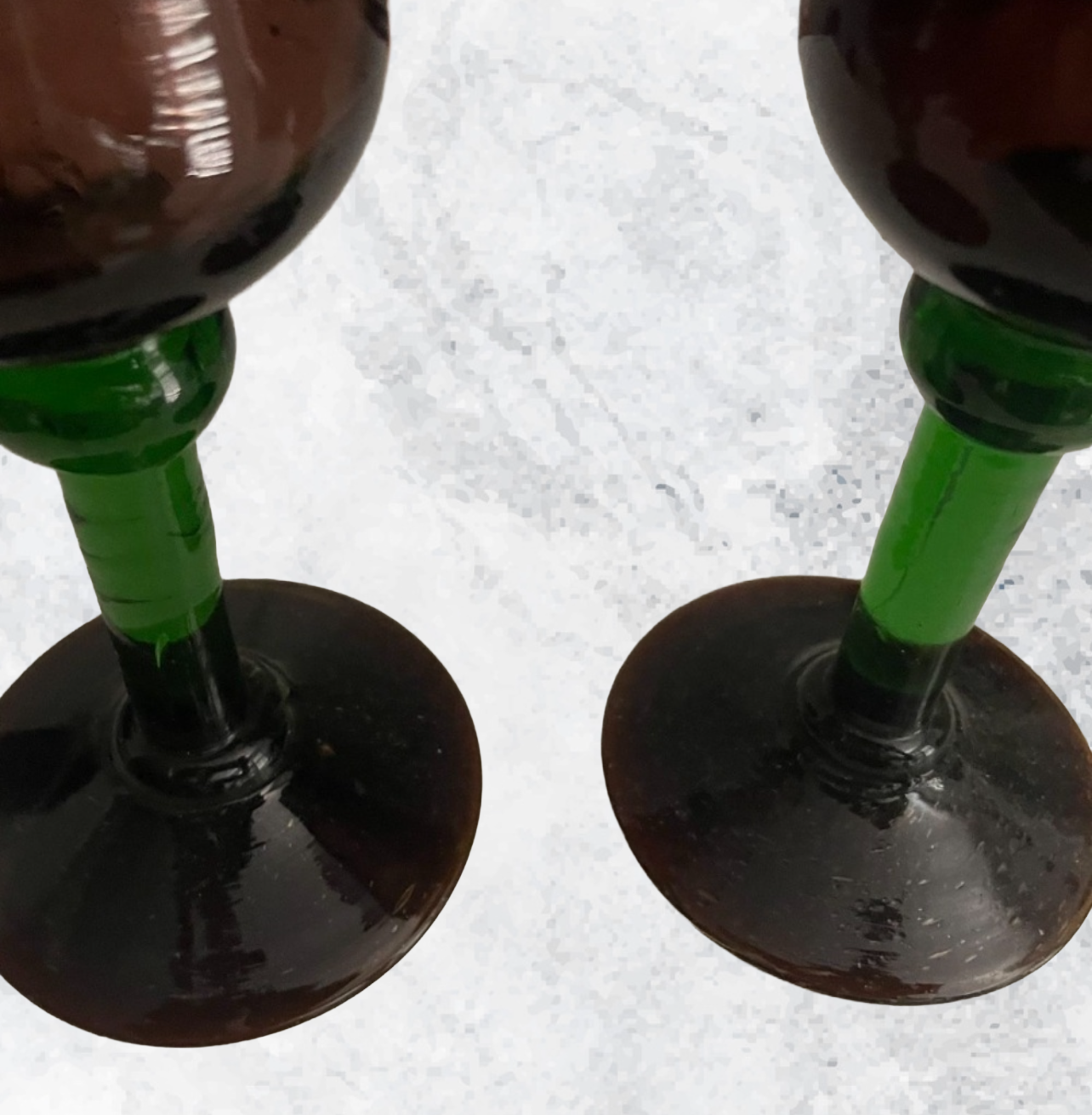 Two identical wine glasses with green stems on a textured white surface