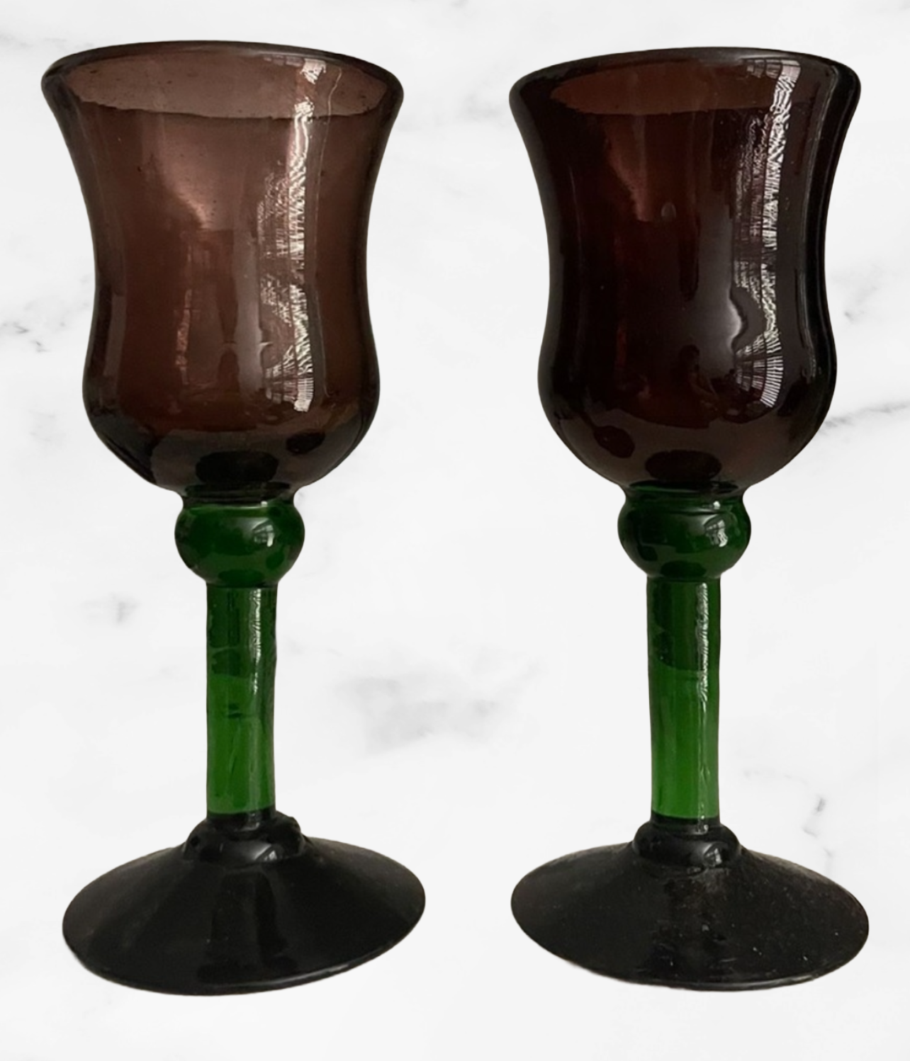 Two brown glass goblets with green stems on a marble surface